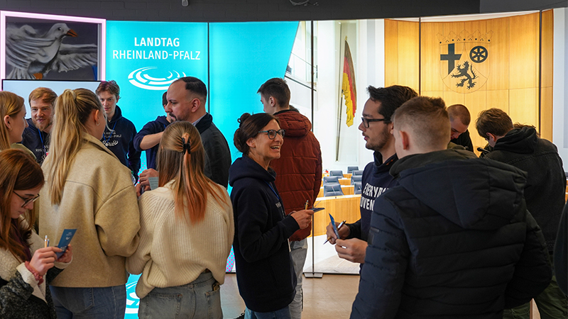 Mehrere Personen im Gespräch miteinander; stehend vor dem Hintergrund des Plenarsaals für das Projekt 