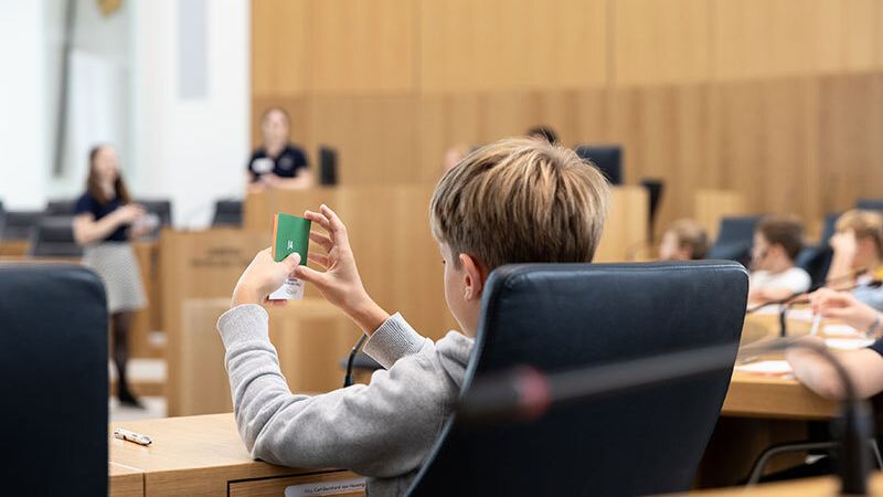 Im Zuge des Grundschulprogramms findet auch ein Planspiel im Plenarsaal statt. Ein Kind hält eine "Ja" Abstimmungskarte in der Hand.