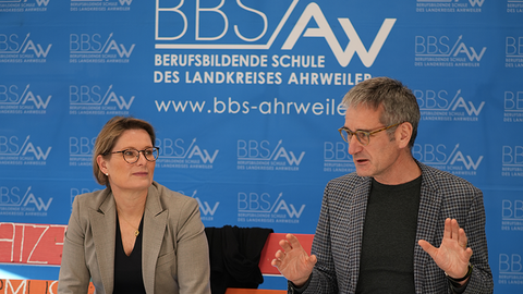 Bildungsministerin Stefanie Hubig und Landtagspräsident Hendrik Hering im Gespräch vor dem Logo der BBS Ahrweiler.