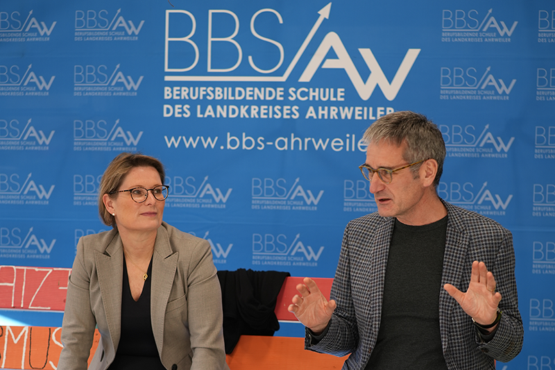 Bildungsministerin Stefanie Hubig und Landtagspräsident Hendrik Hering im Gespräch vor dem Logo der BBS Ahrweiler.